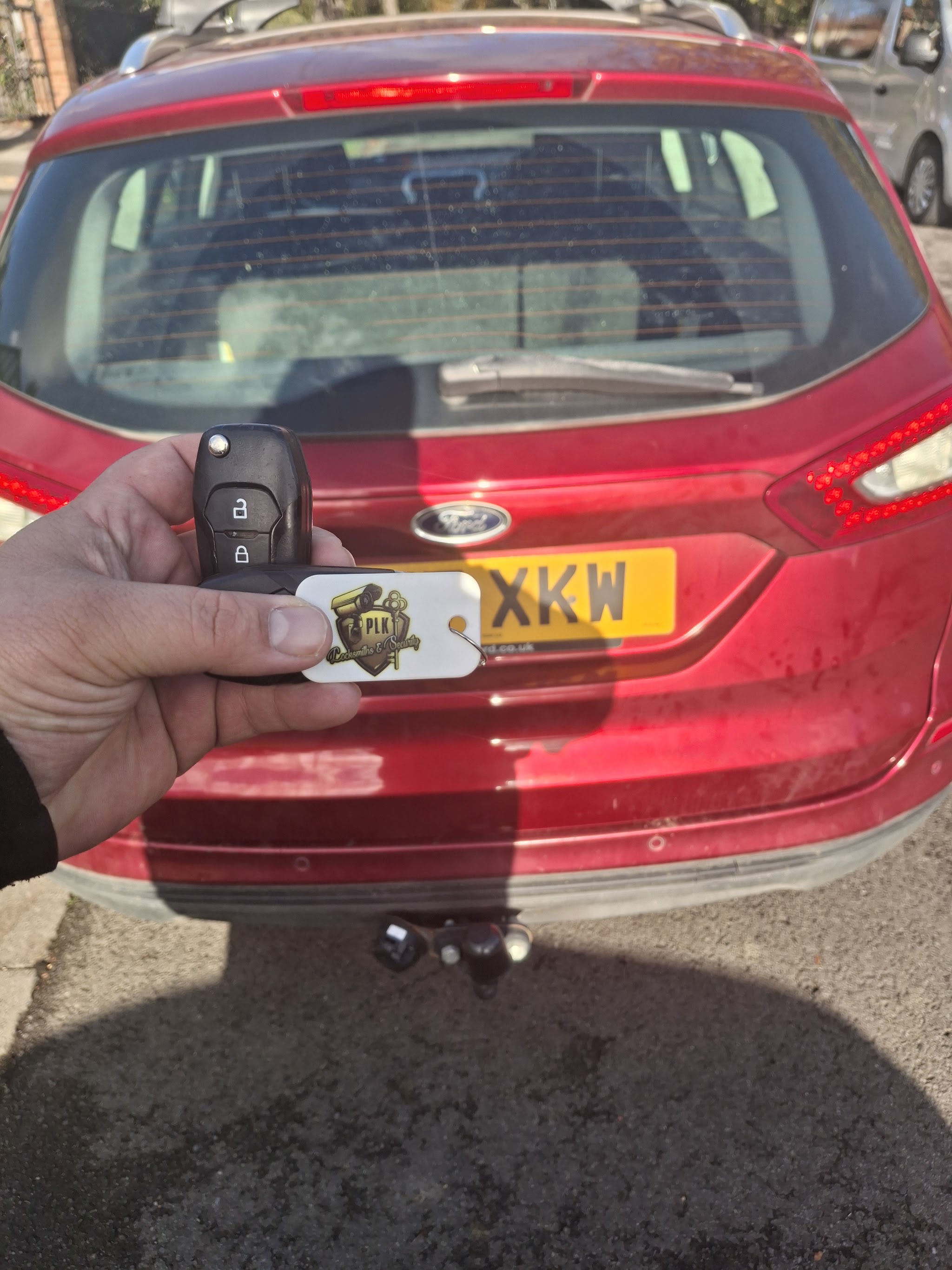 A Ford remote key with the PLK keyring, held up in front of the car